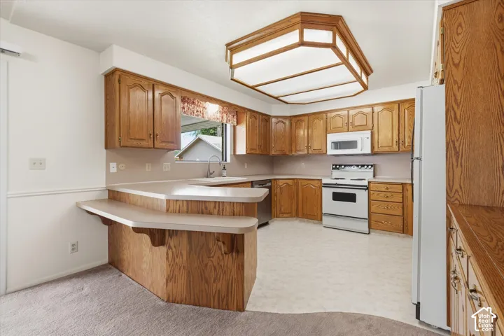 Kitchen featuring wood cabinetry, white appliances, a double-tiered breakfast bar, and a built-in ceiling light fixture