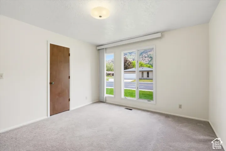 Bright room featuring three large windows, neutral wall paint, and grey carpeting