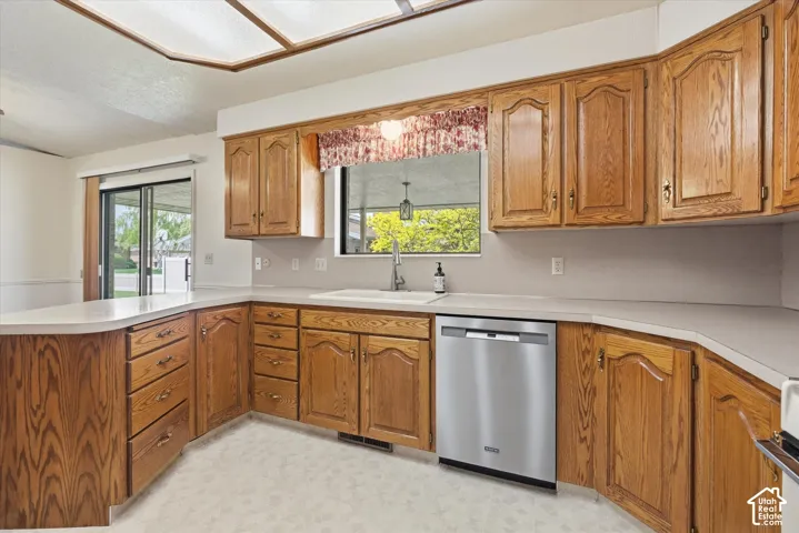 Kitchen featuring wood-finish cabinetry with brass-tone hardware, light-toned countertops, a stainless steel dishwasher, and an undermount sink