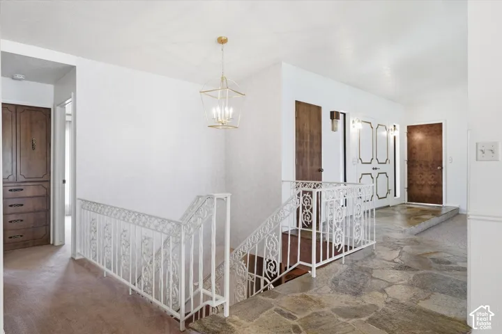 Flagstone flooring extending into the hallway, featuring a white wrought iron railing and a contemporary gold-finished chandelier