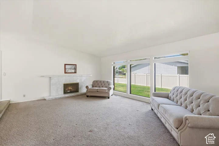 Spacious interior featuring a white-painted fireplace with a stone surround, a large picture window, and light-colored carpeting