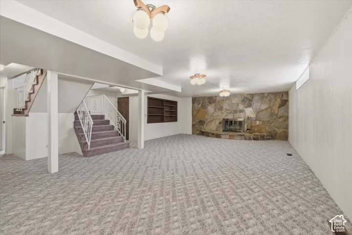 Spacious carpeted room featuring a stone-clad fireplace, integrated shelving, white paneled walls, and overhead lighting