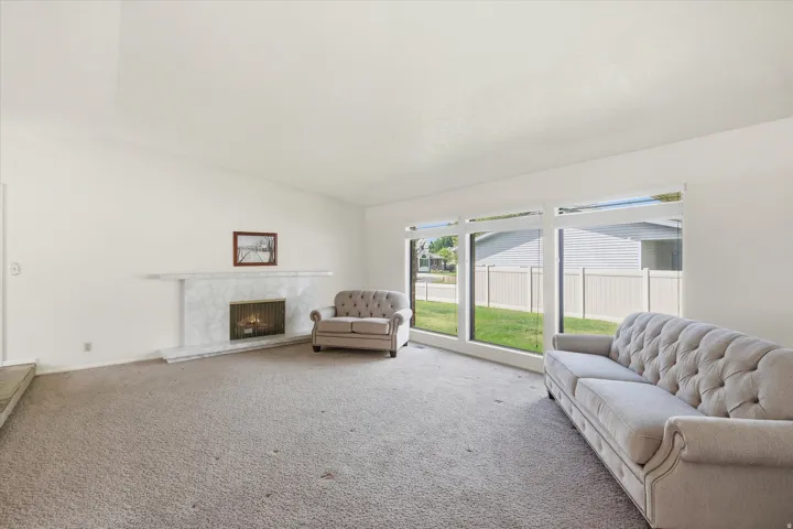 Spacious interior featuring a white-painted fireplace with a stone surround, a large picture window, and light-colored carpeting