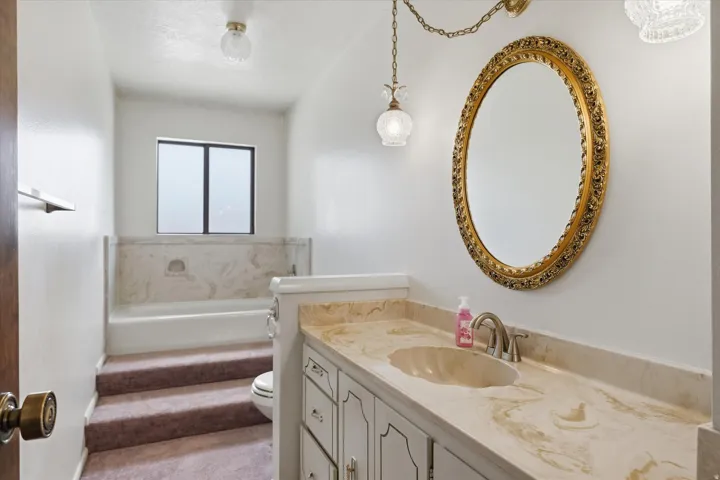 Vanity featuring a stone countertop with an integrated sink and a classic gold-framed mirror