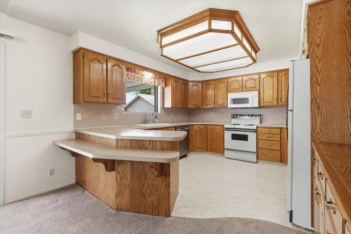 Kitchen featuring wood cabinetry, white appliances, a double-tiered breakfast bar, and a built-in ceiling light fixture