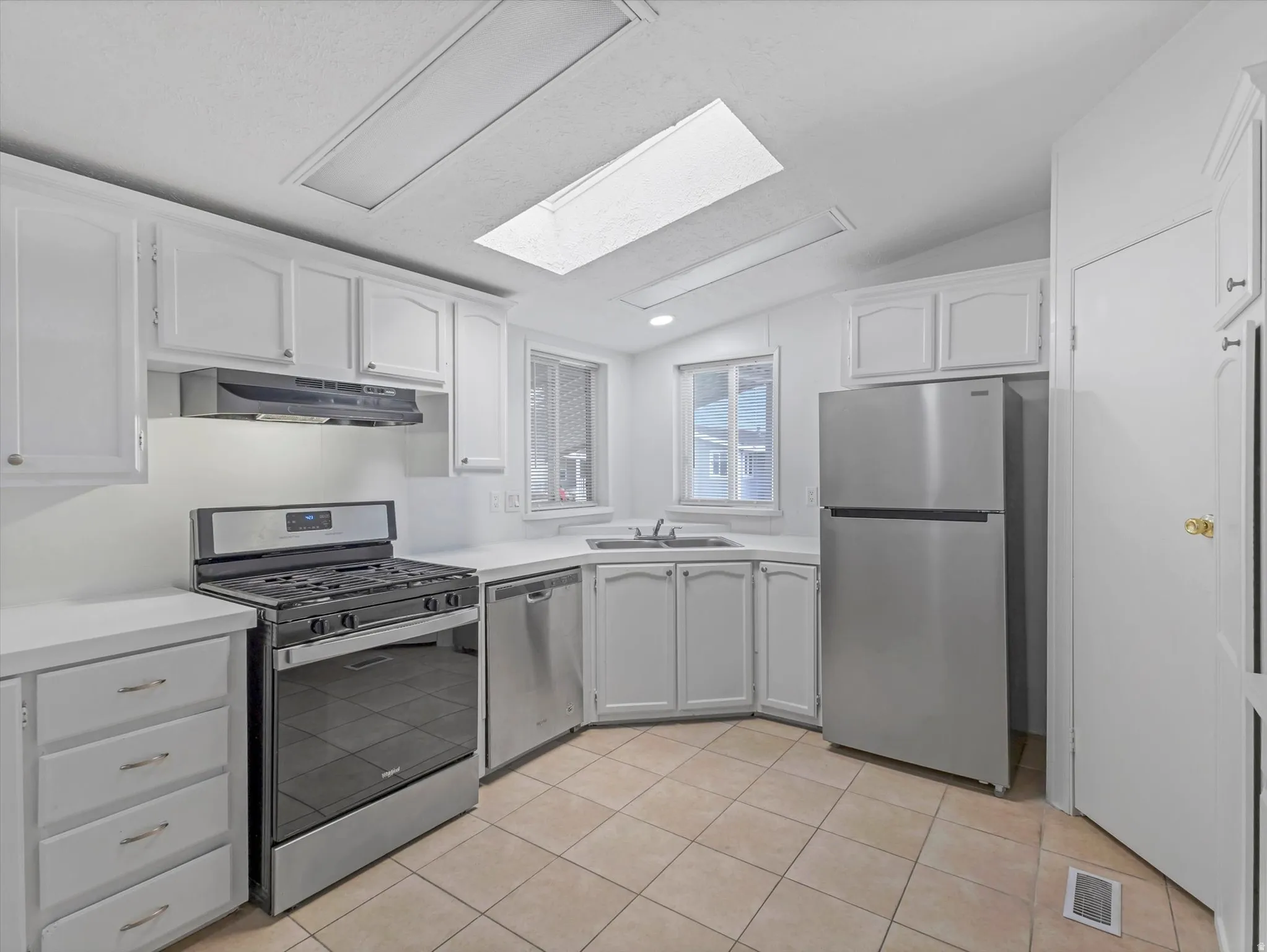 Kitchen featuring white cabinetry, light-toned tile flooring, stainless steel appliances, white countertops, and a skylight