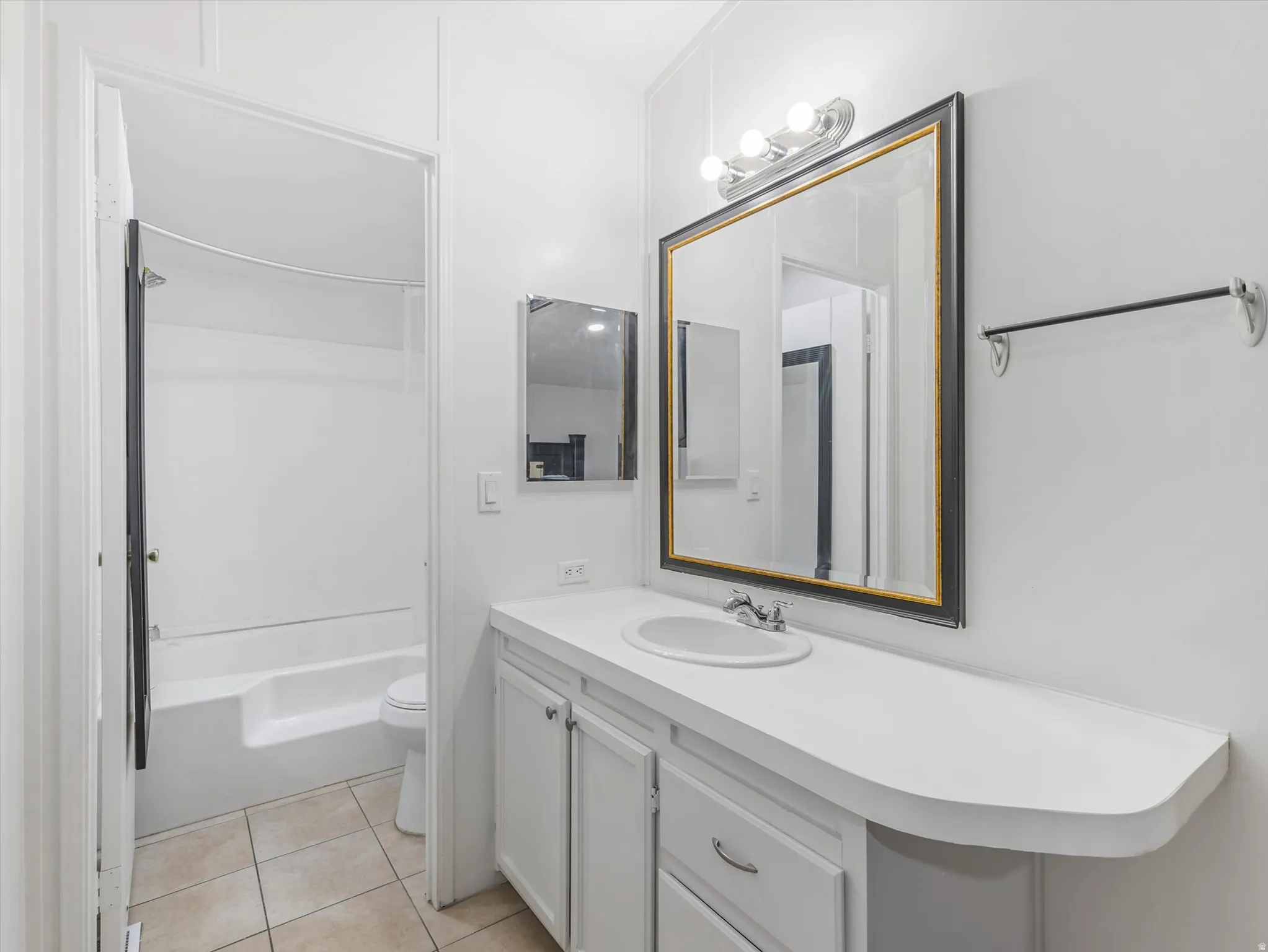 Bathroom featuring a vanity with an integrated sink, a rectangular framed mirror, a three-bulb vanity light fixture, and a tiled floor