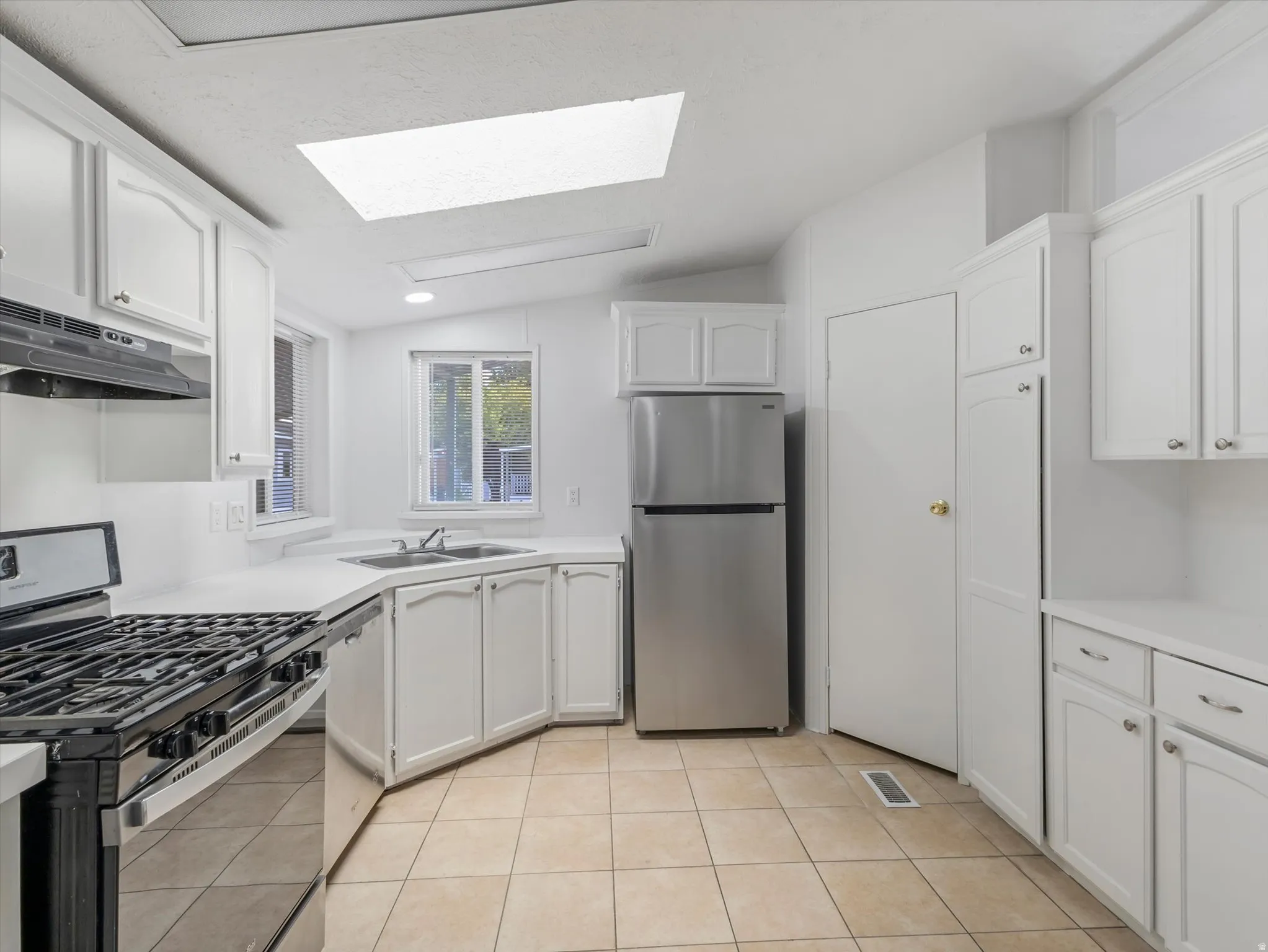 Kitchen featuring white cabinetry with arch details, stainless steel appliances, a gas range, a skylight, and neutral square tile flooring