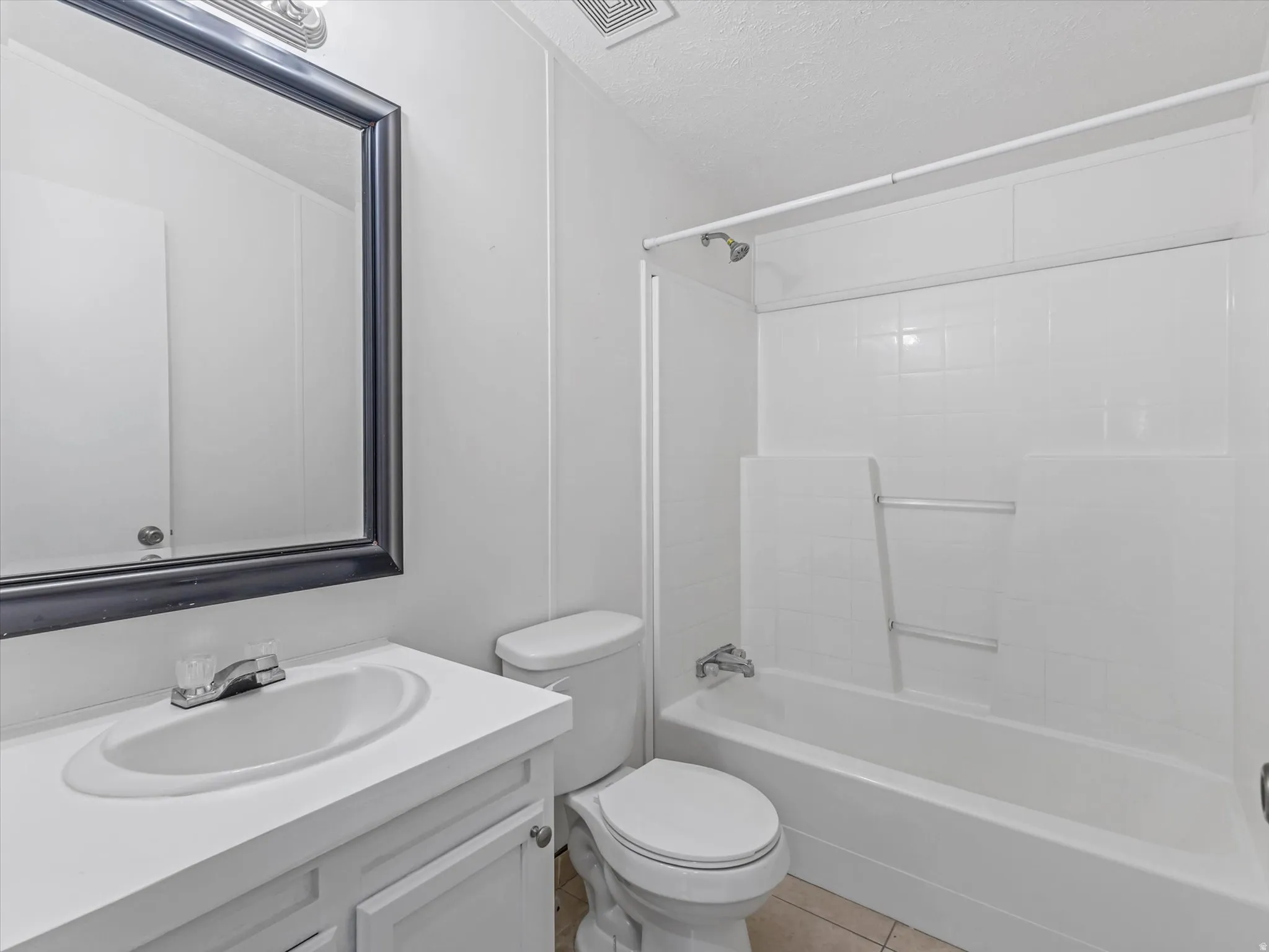 Bathroom featuring a white vanity with integrated sink, chrome faucet, framed mirror, and a tiled shower/tub combination