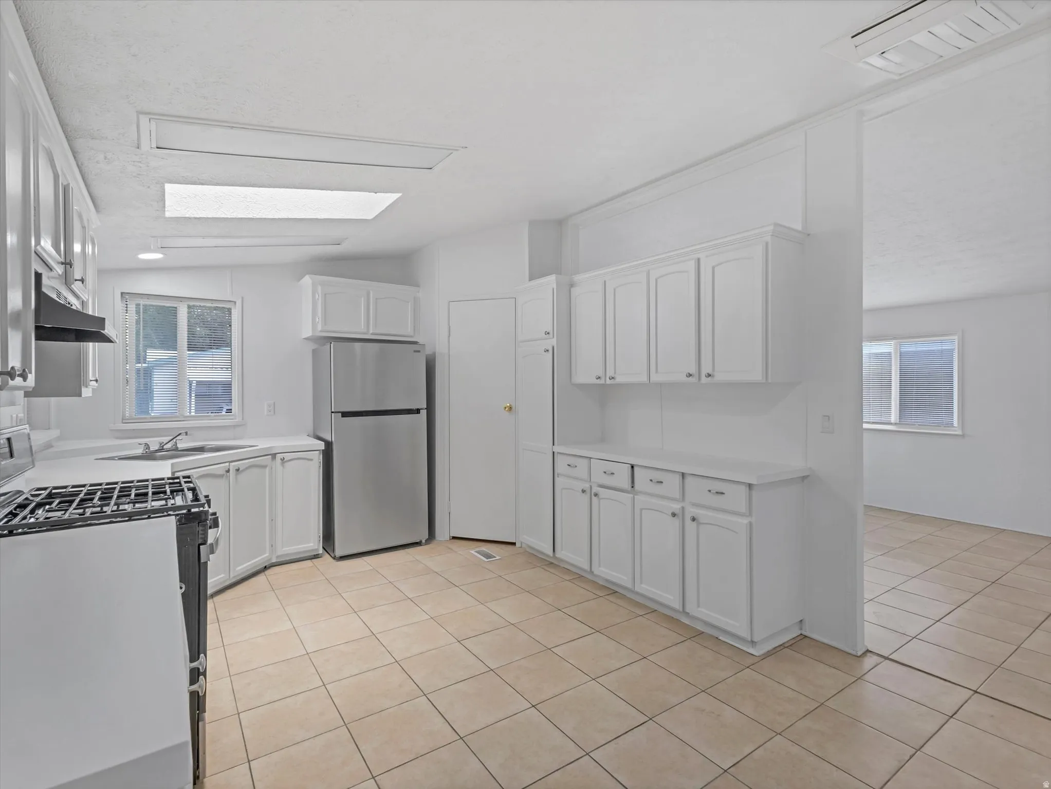 Kitchen featuring white cabinetry, tile flooring, stainless steel refrigerator, white countertops, and a built-in range