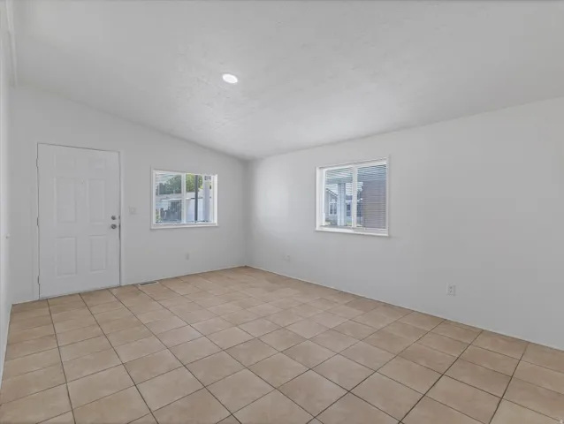 Neutral tile flooring spanning the room, white walls, and a matching white entry door