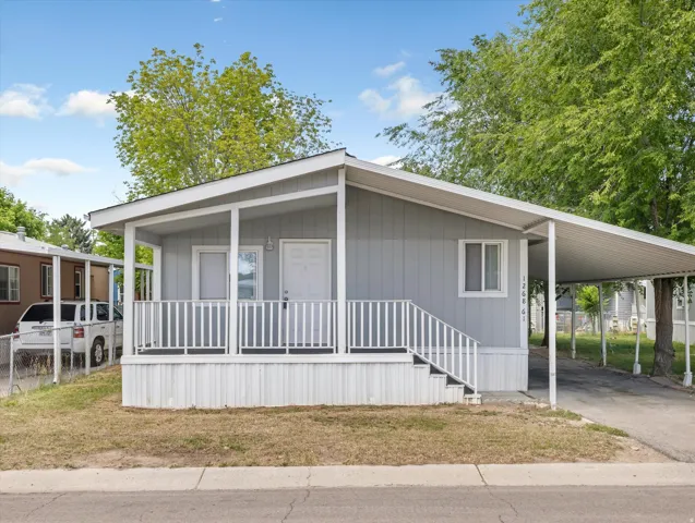 Light gray manufactured home with white trim, a covered front porch, and an attached carport