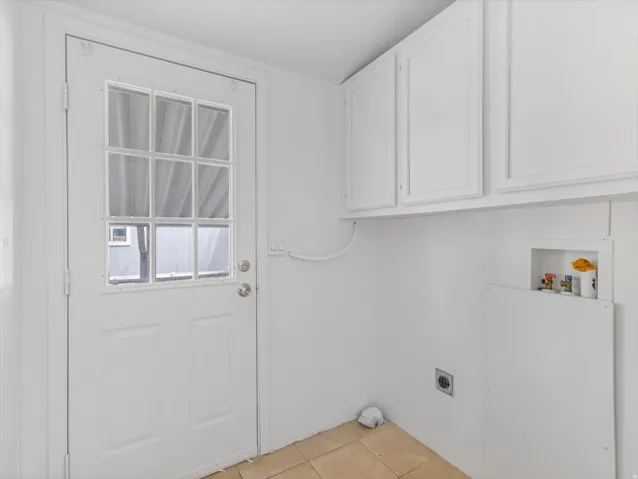 Utility room featuring a white paneled door with nine-light window, light-toned tile flooring, white upper cabinetry, and dedicated laundry hookups