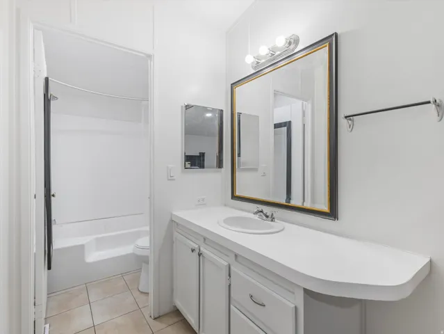 Bathroom featuring a vanity with an integrated sink, a rectangular framed mirror, a three-bulb vanity light fixture, and a tiled floor