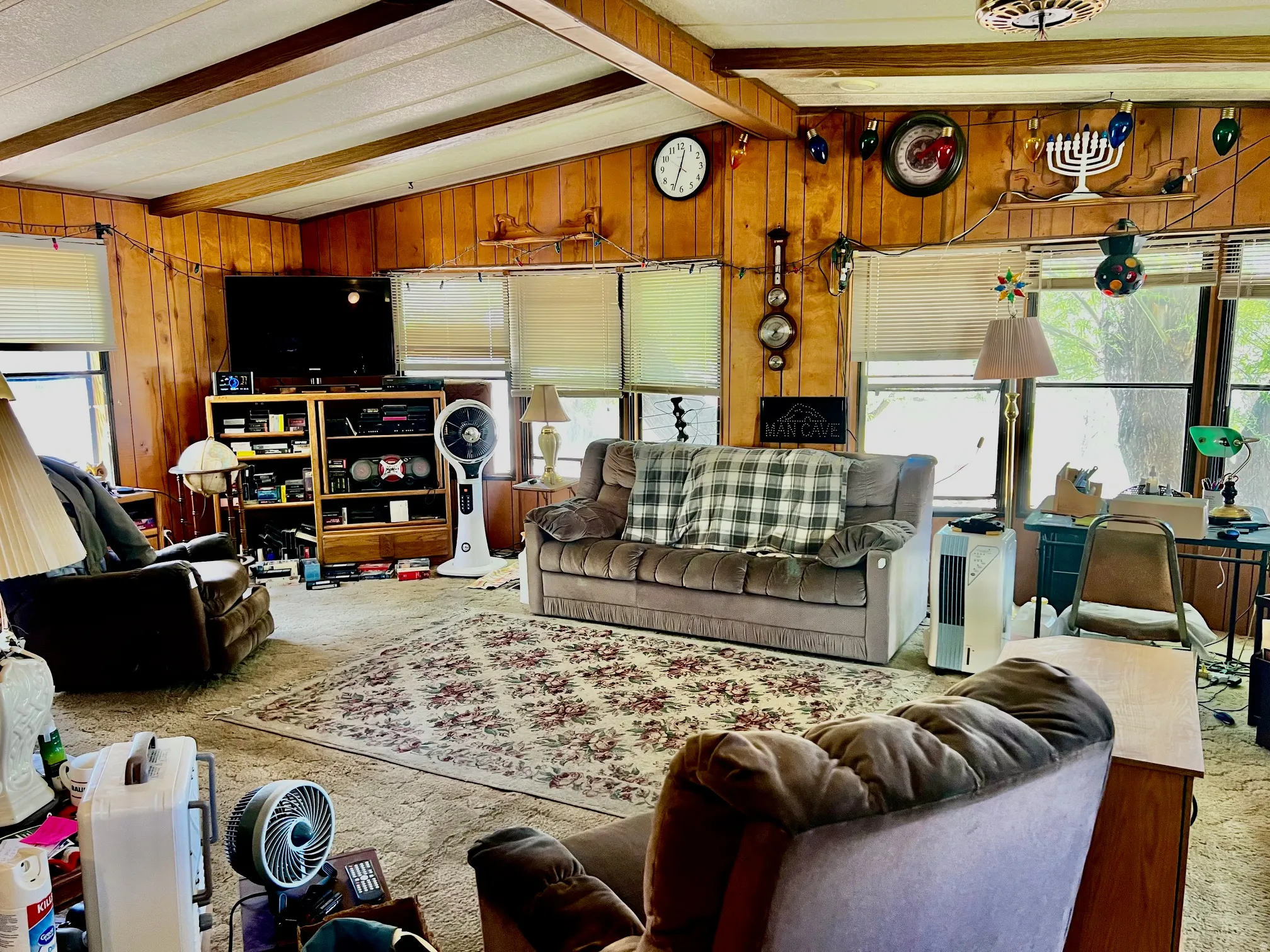Living area featuring wood paneling, wood-finish ceiling beams, and multiple windows with blinds
