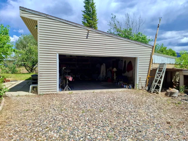Detached garage with horizontal siding, an open overhead door, and a gravel driveway
