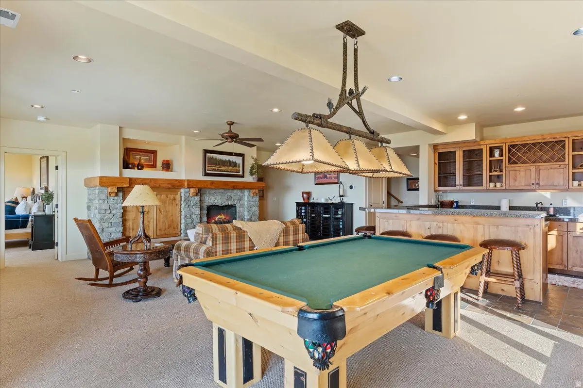 Recreational space featuring a built-in wet bar with wood cabinetry and a stone countertop, a stone fireplace with a substantial wood mantel, recessed lighting, and a ceiling fan