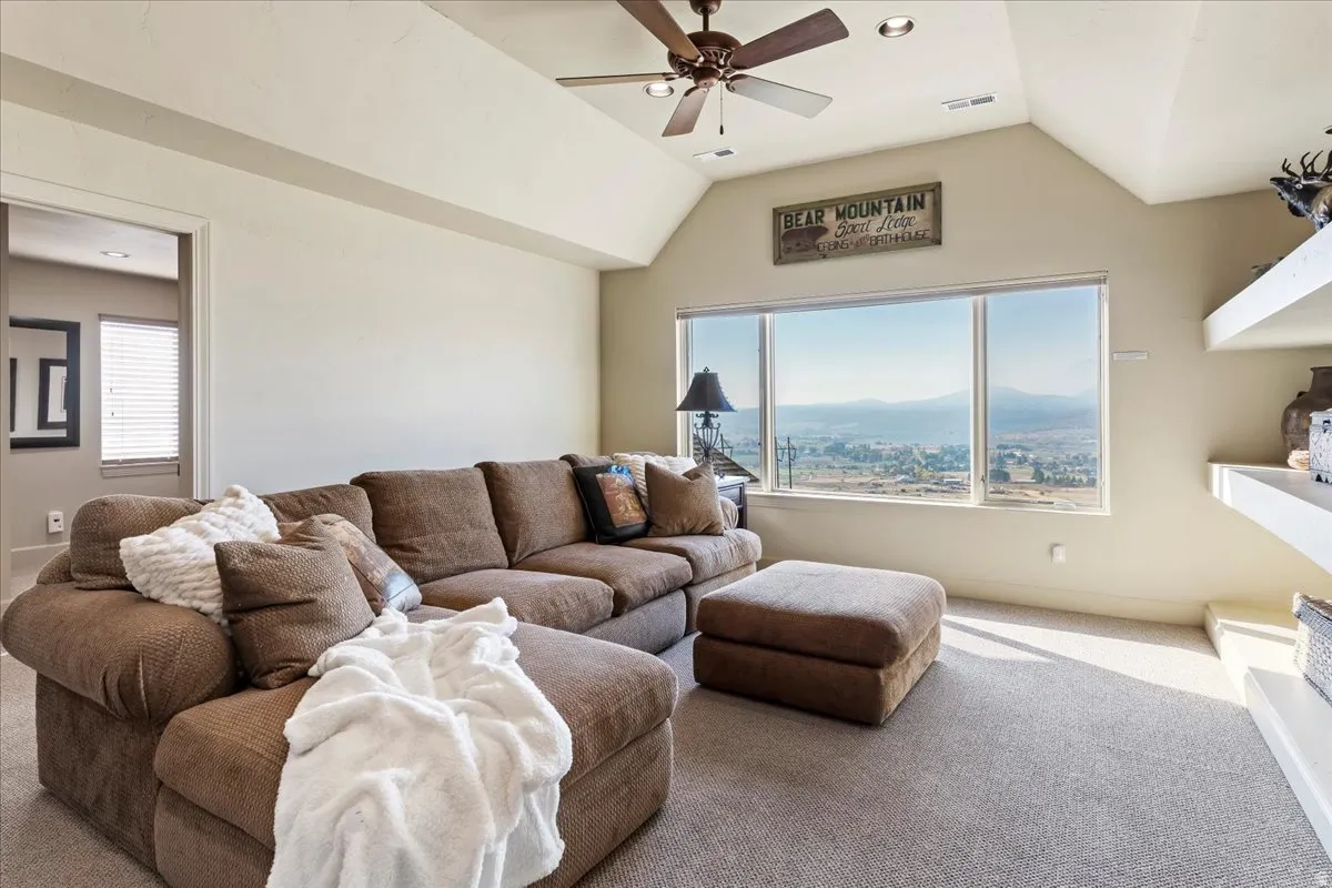 Spacious room featuring a large window with distant mountain and city scenery, vaulted ceilings, a ceiling fan, recessed lighting, and wall-mounted shelving