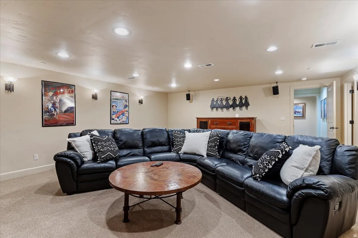 Spacious entertainment room featuring recessed ceiling lighting, wall-mounted sconces, and neutral carpeting