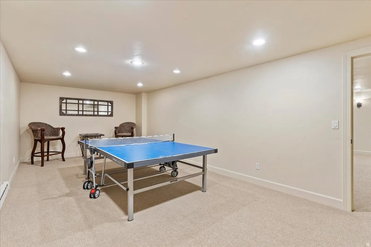 Spacious recreation room featuring recessed lighting, neutral carpeting, and a broad doorway opening into an additional carpeted area