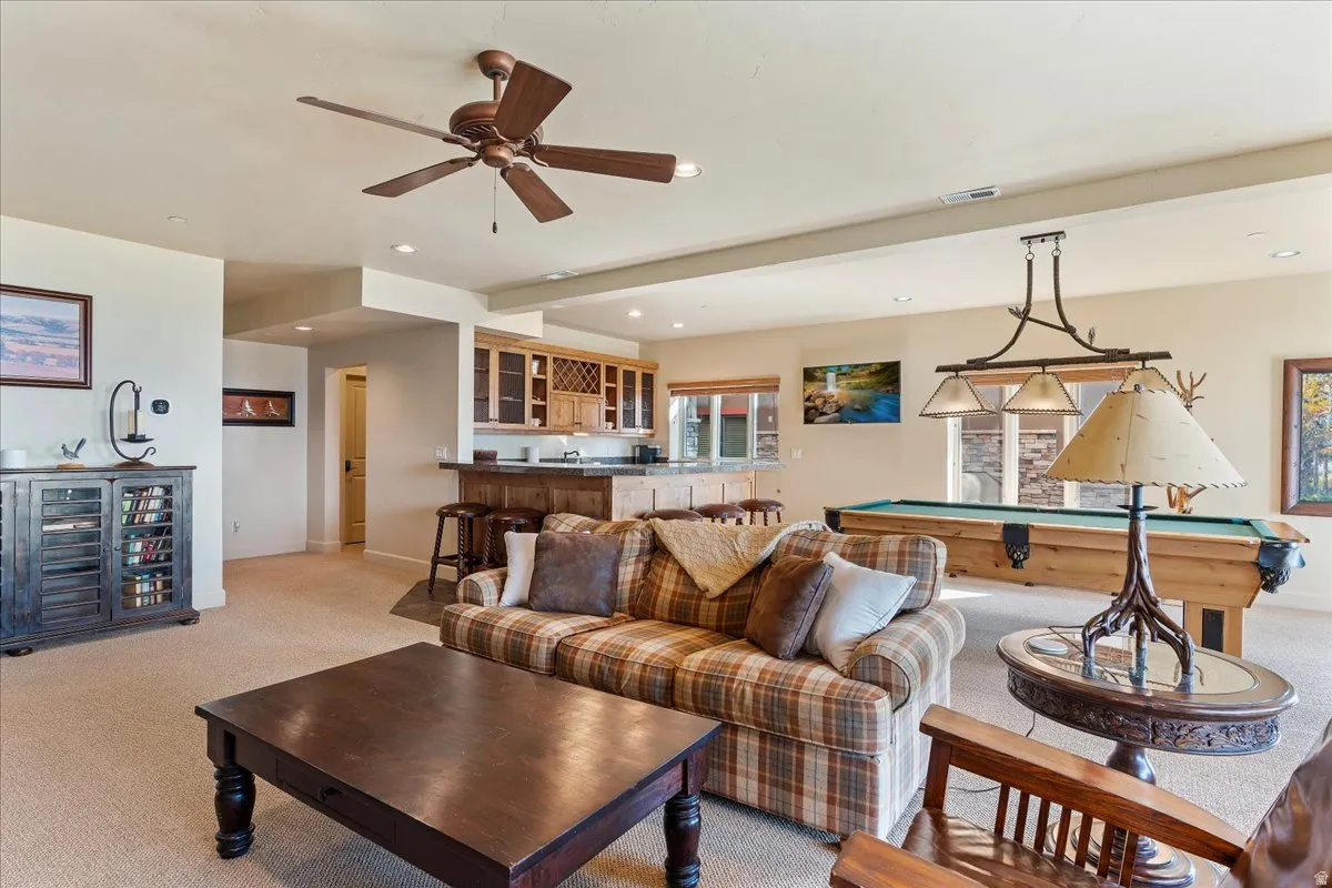 Open-concept recreation room featuring a built-in wet bar with wood cabinetry, a recessed bar area with pendant lighting, a ceiling fan, and carpeted flooring
