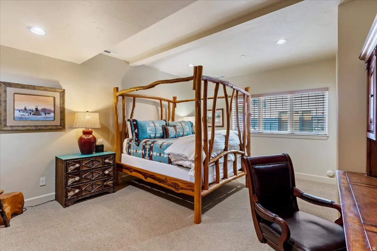 Carpeted bedroom featuring a rustic wood-frame bed, recessed lighting, and a window with horizontal blinds