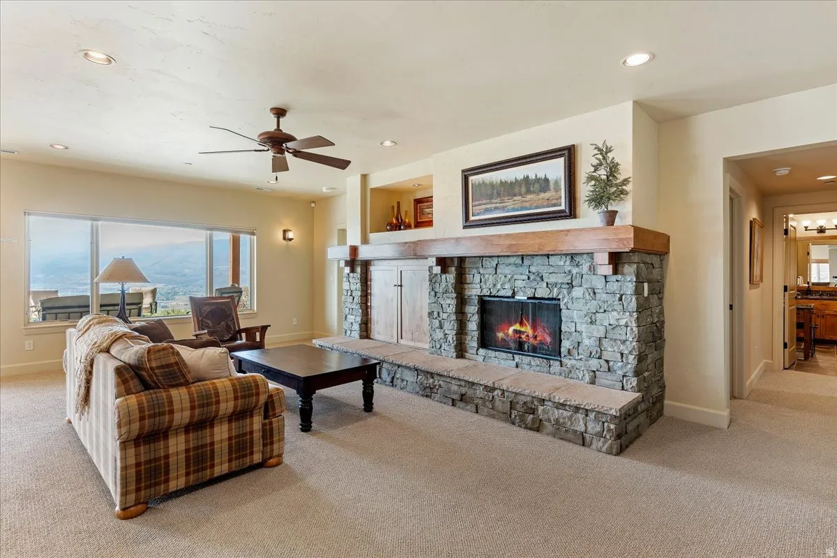 Spacious living area featuring a floor-to-ceiling stone fireplace with a substantial wood mantel, carpeted flooring, large picture windows, and recessed lighting