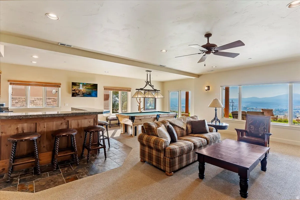 Entertainment space featuring a wood-panel wet bar with stone-finish countertop, recessed lighting, and a ceiling fan