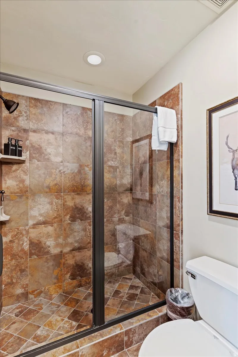 Glass-enclosed shower with a bronze frame, textured brown and rust-colored tile, built-in bench, and recessed lighting
