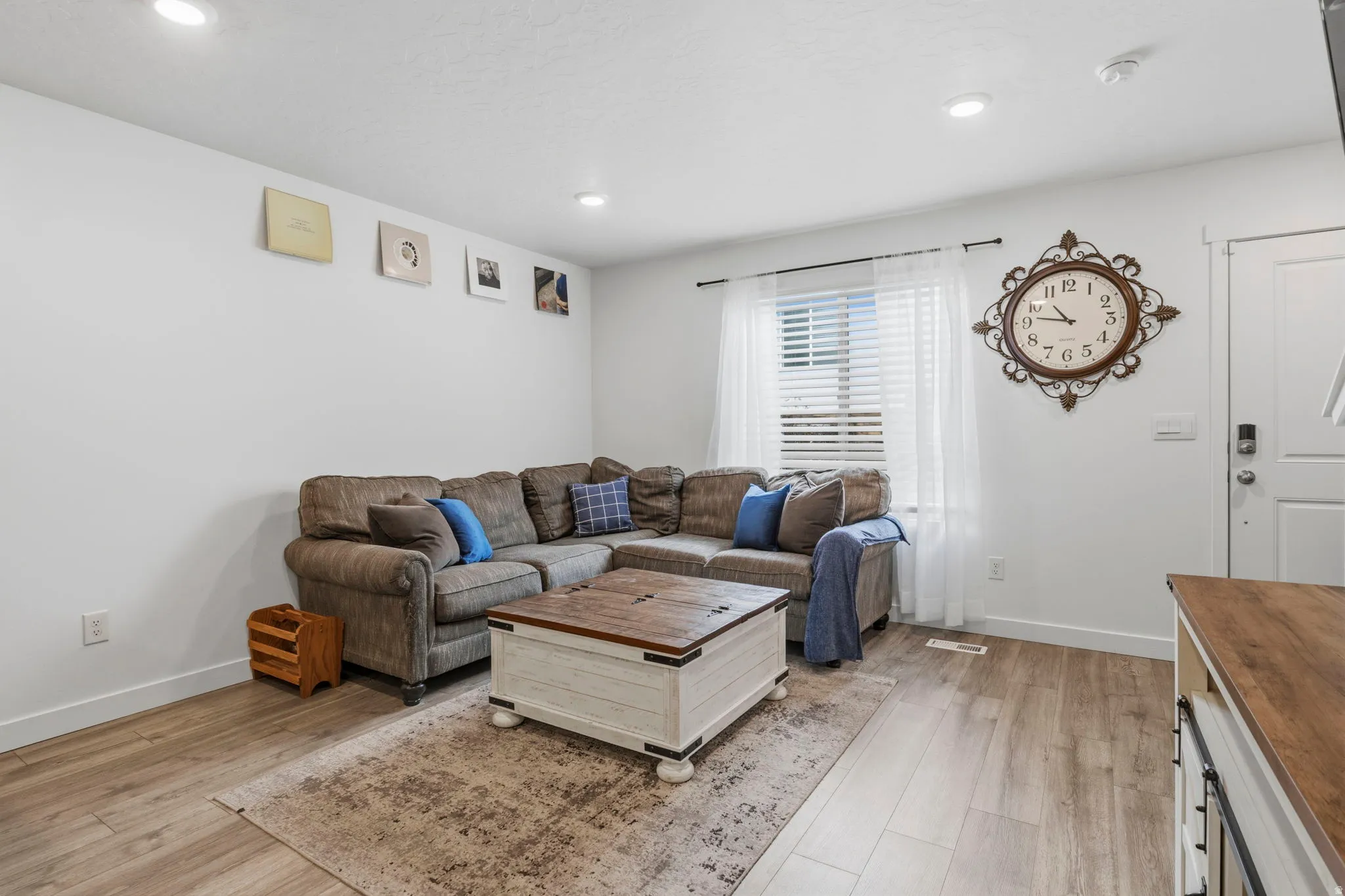 Open-concept living area featuring wood-finish flooring, recessed lighting, white walls, and a prominent window with blinds