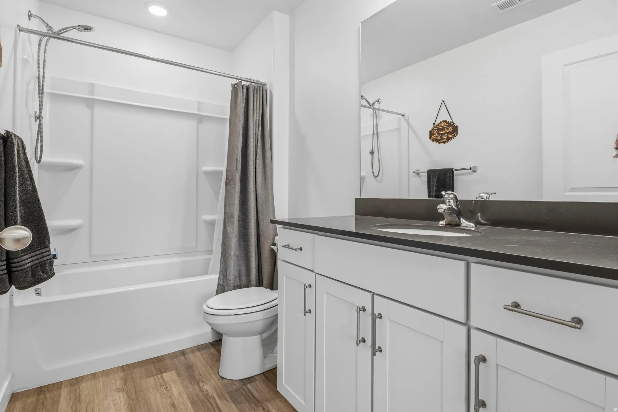 White vanity with a dark countertop and integrated sink, chrome faucet, and full-width mirror