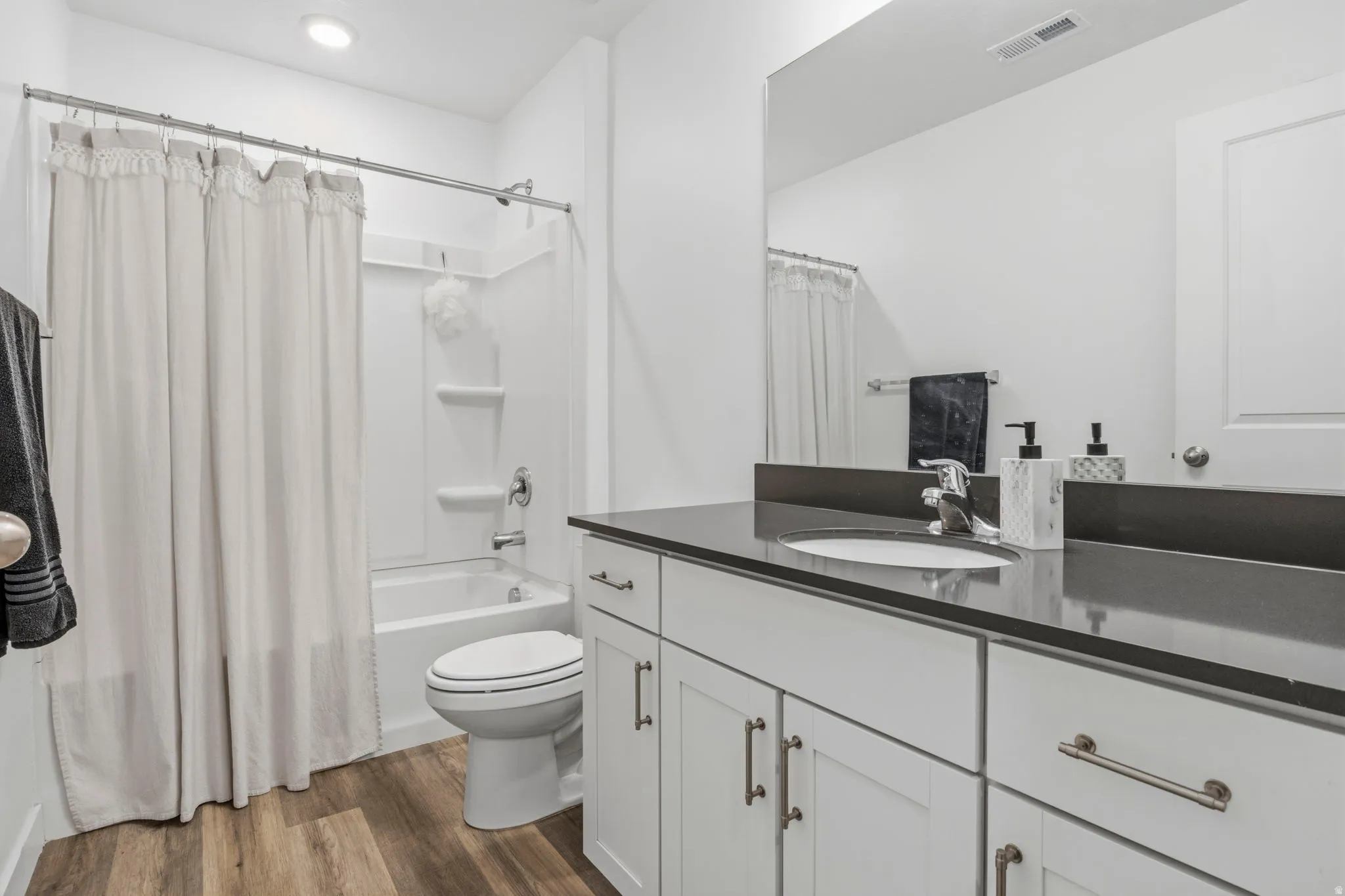 Master Full bathroom featuring a white vanity with slab doors and drawers, a dark countertop with an integrated sink, a large mirror, a white toilet, and wood-finish flooring