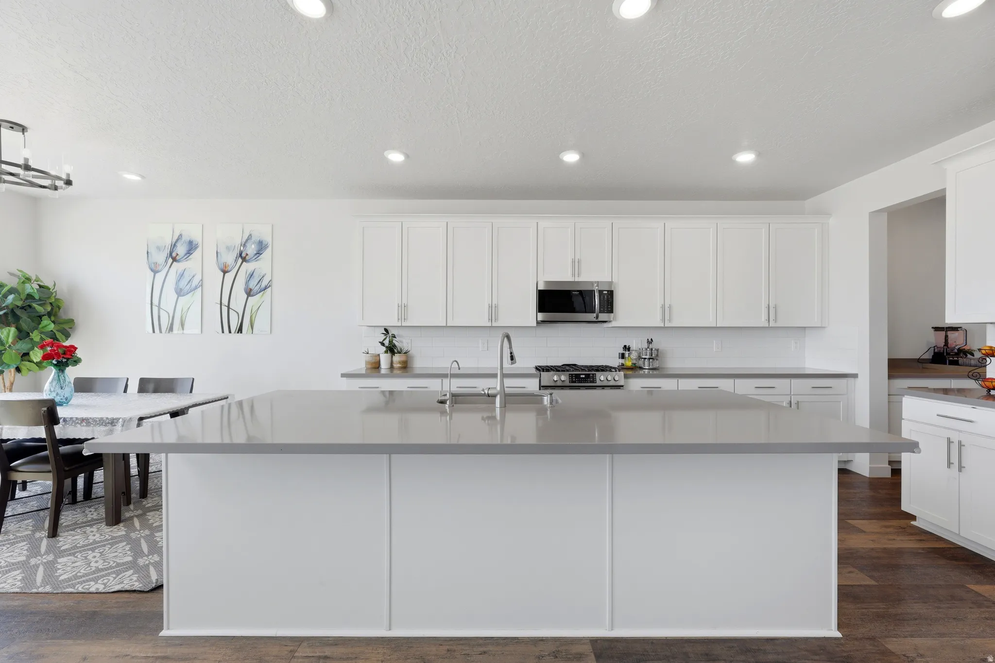 Contemporary kitchen featuring a spacious island with a solid surface countertop, white shaker-style cabinetry, stainless steel appliances, a subway tile backsplash, and recessed lighting