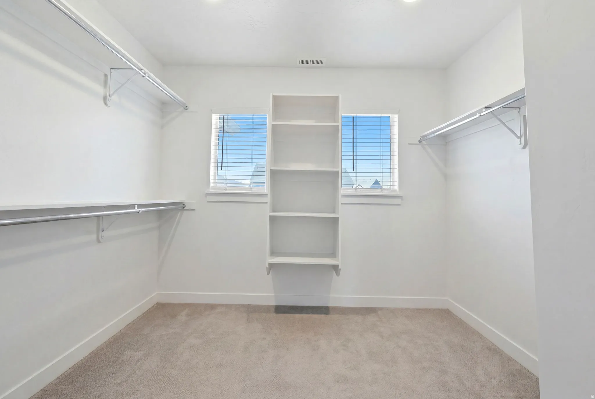 Spacious walk-in closet featuring built-in shelving, two windows with blinds, and ample hanging rod space