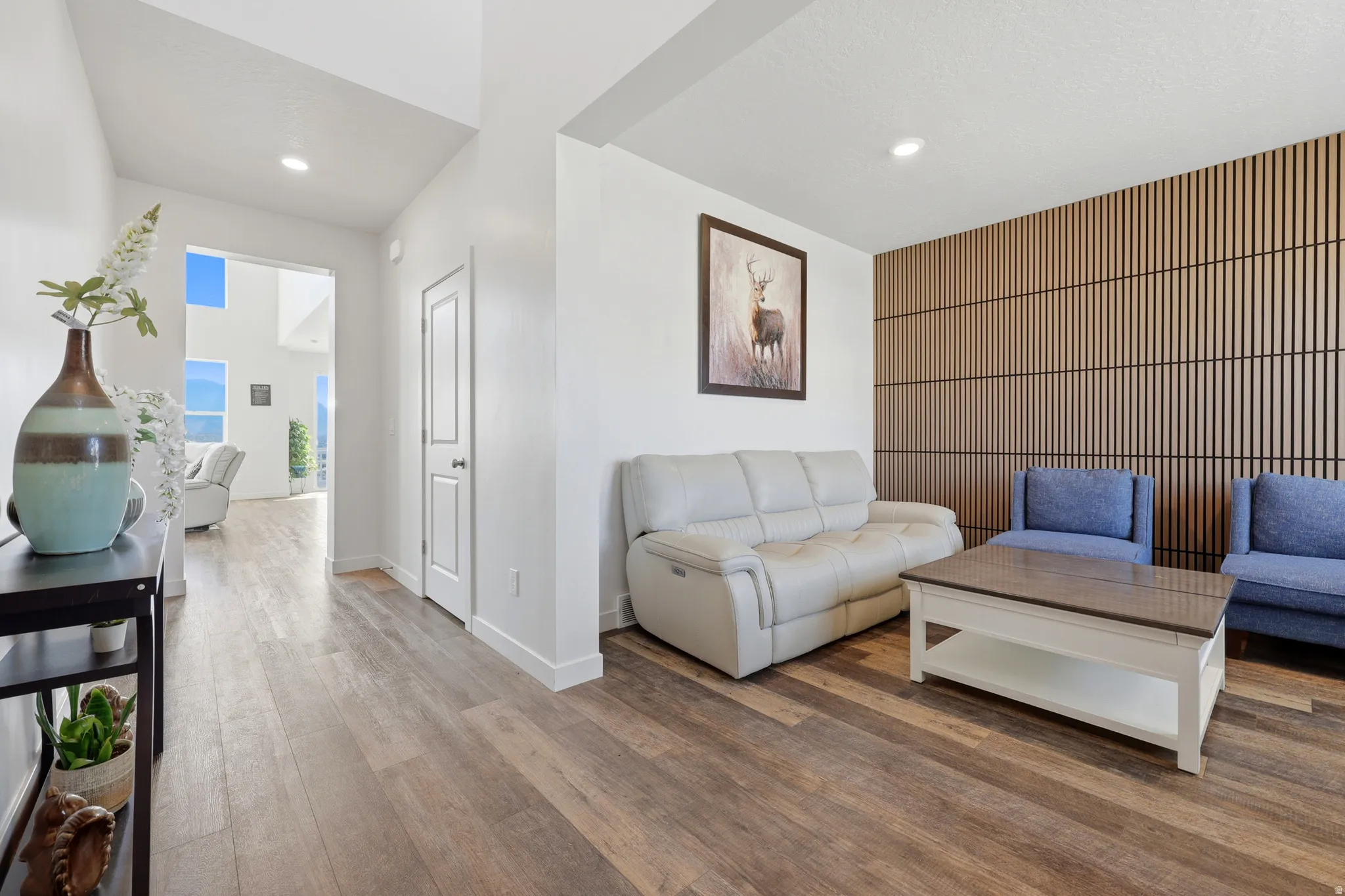 Spacious living area featuring wood-finish flooring, a contemporary slatted accent wall, recessed lighting, and a white interior door