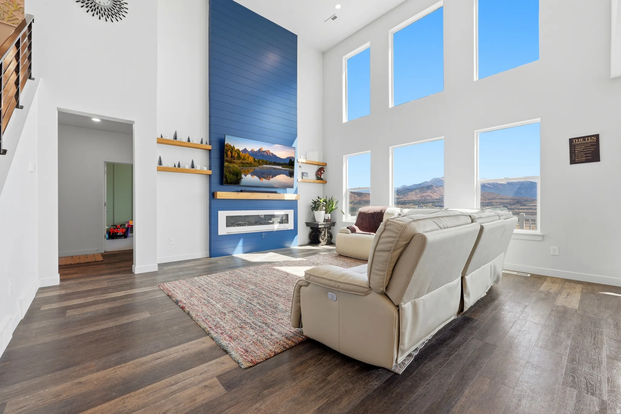 Two-story living area featuring a blue shiplap accent wall with an integrated linear fireplace, wood-finish flooring, and multiple large windows