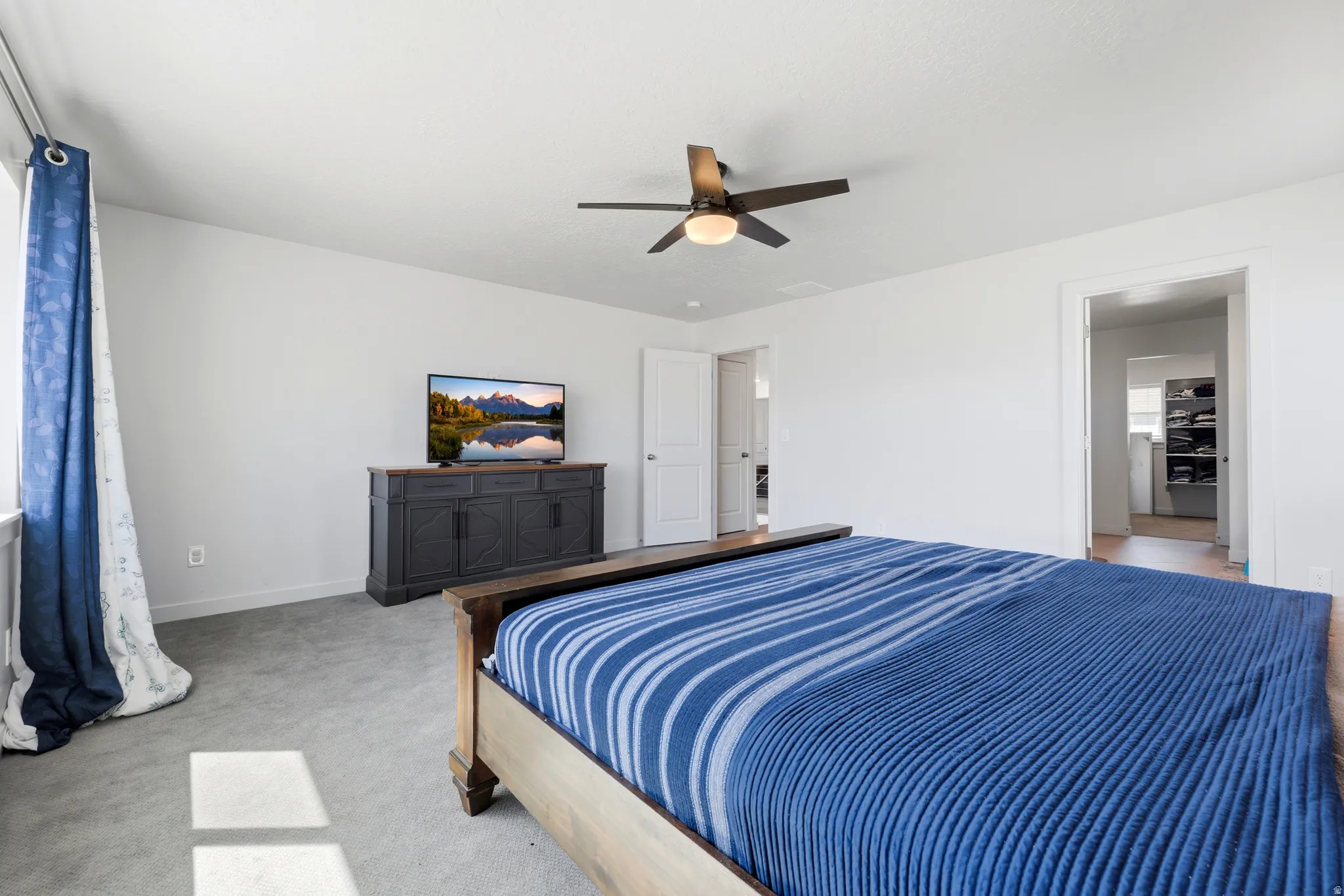 Spacious room featuring light gray carpeting, neutral wall finishes, a window with natural light, and a ceiling fan with integrated lighting