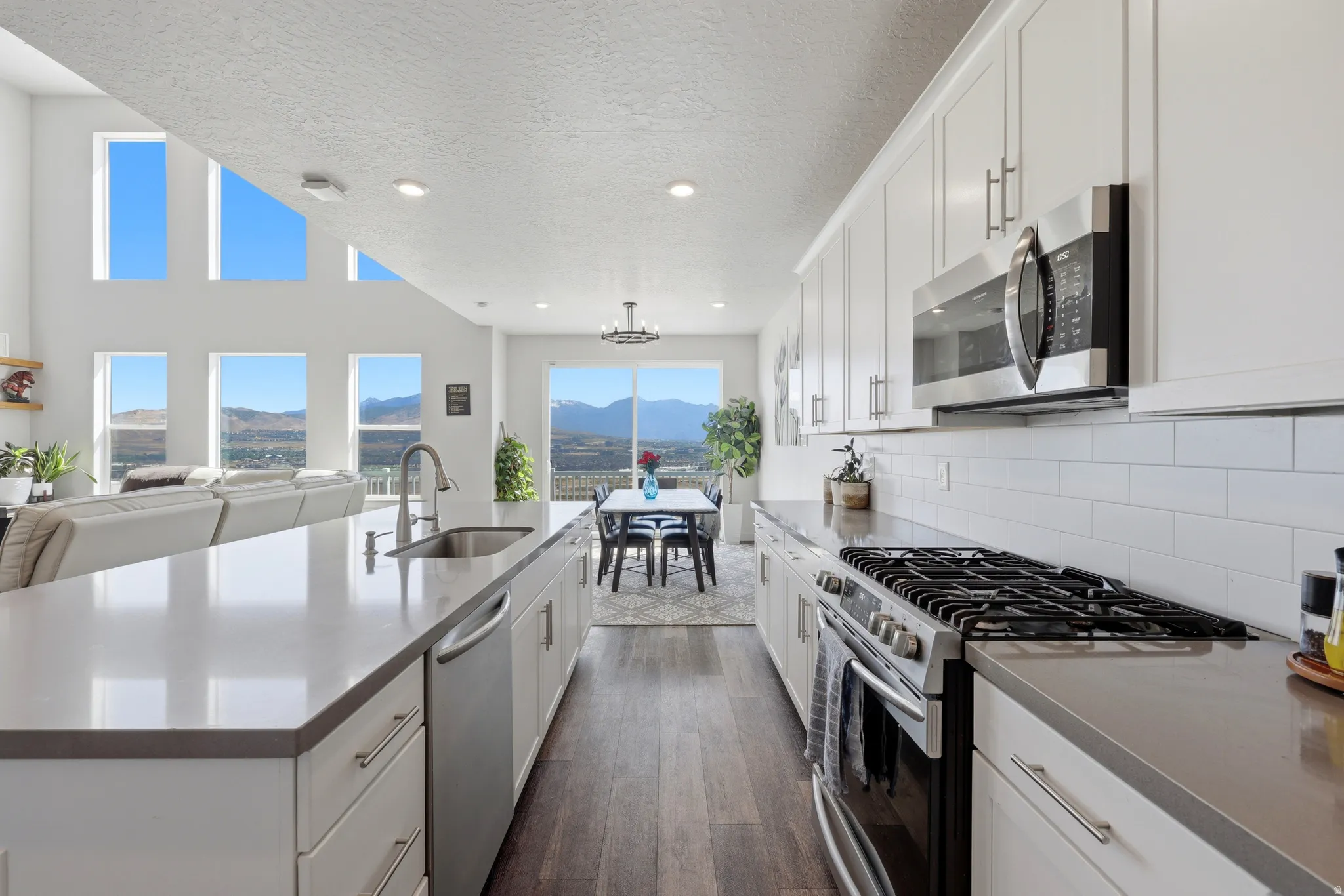 Contemporary kitchen featuring an expansive island with an undermount sink, stainless steel appliances, white subway tile backsplash, and wood-finish flooring