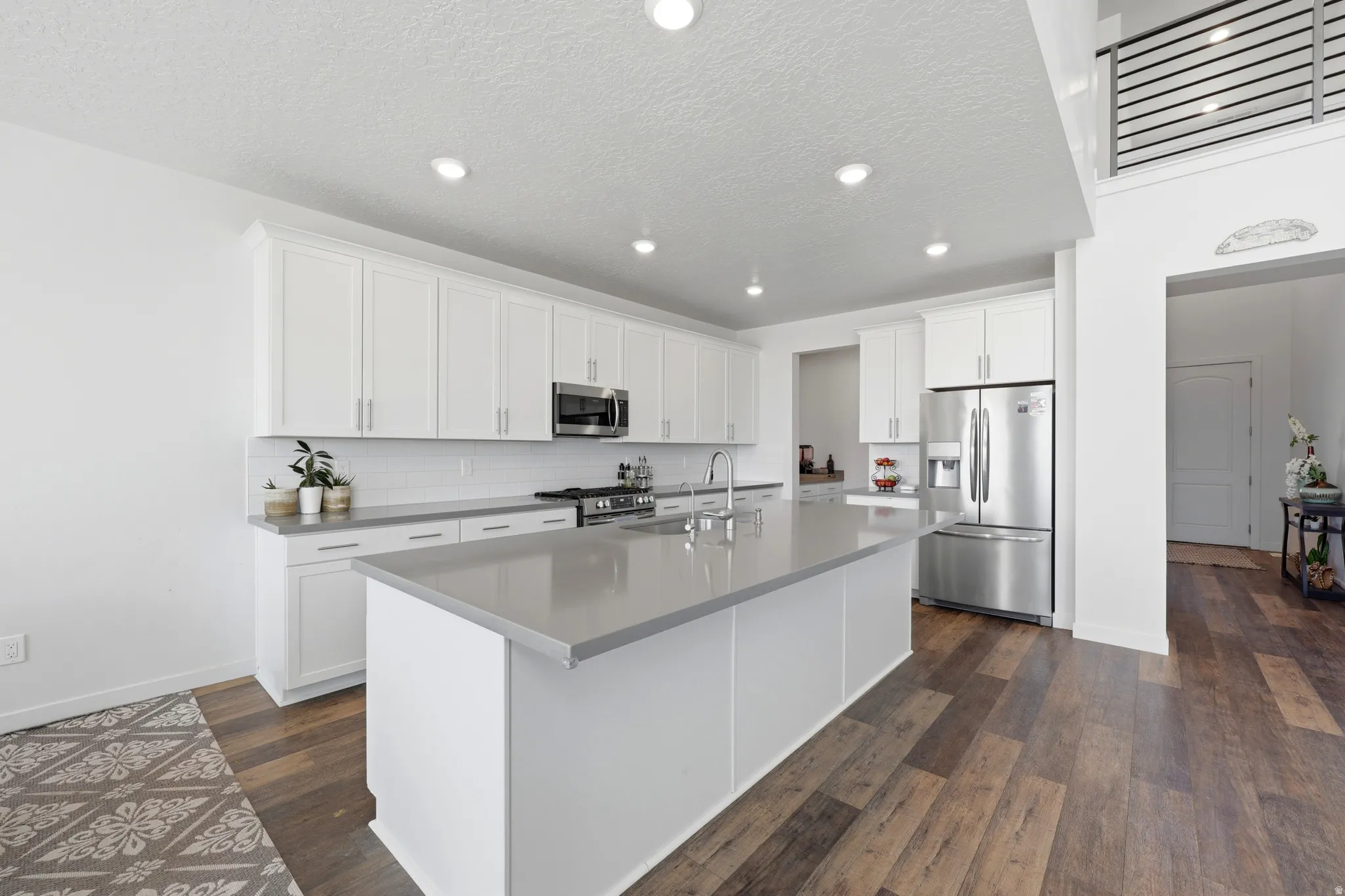Modern kitchen featuring white shaker cabinetry, stainless steel appliances, a large center island with a gray countertop, and wood-finish flooring