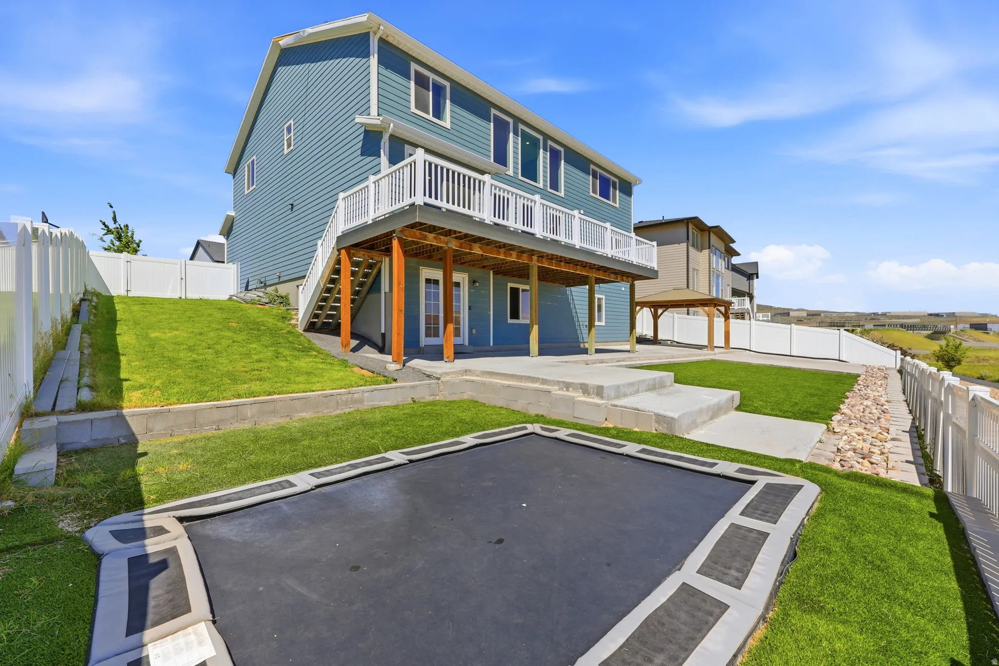 Expansive backyard featuring a built-in trampoline, concrete patio, and a tiered retaining wall