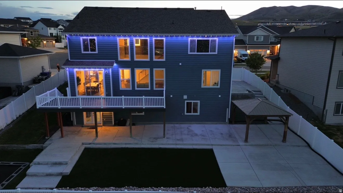 Two-story exterior with blue siding, a ground-level patio, an elevated deck with white railings, a lower artificial turf area, and a standalone gazebo