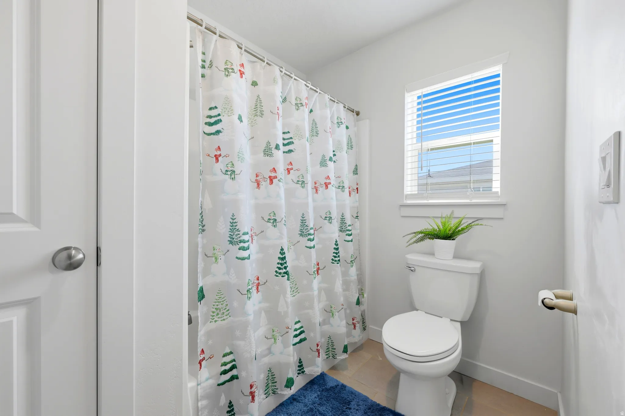 Full bathroom featuring a white toilet, bright window with blinds, and light-toned flooring