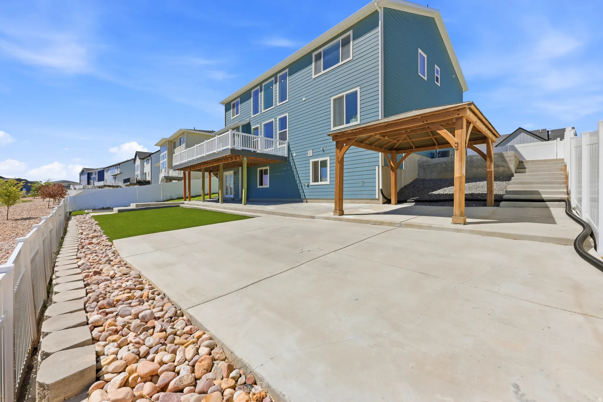 Rear exterior featuring blue siding, a ground-level patio, an upper-level deck with white railings, a wooden pergola, and a terraced concrete stairway
