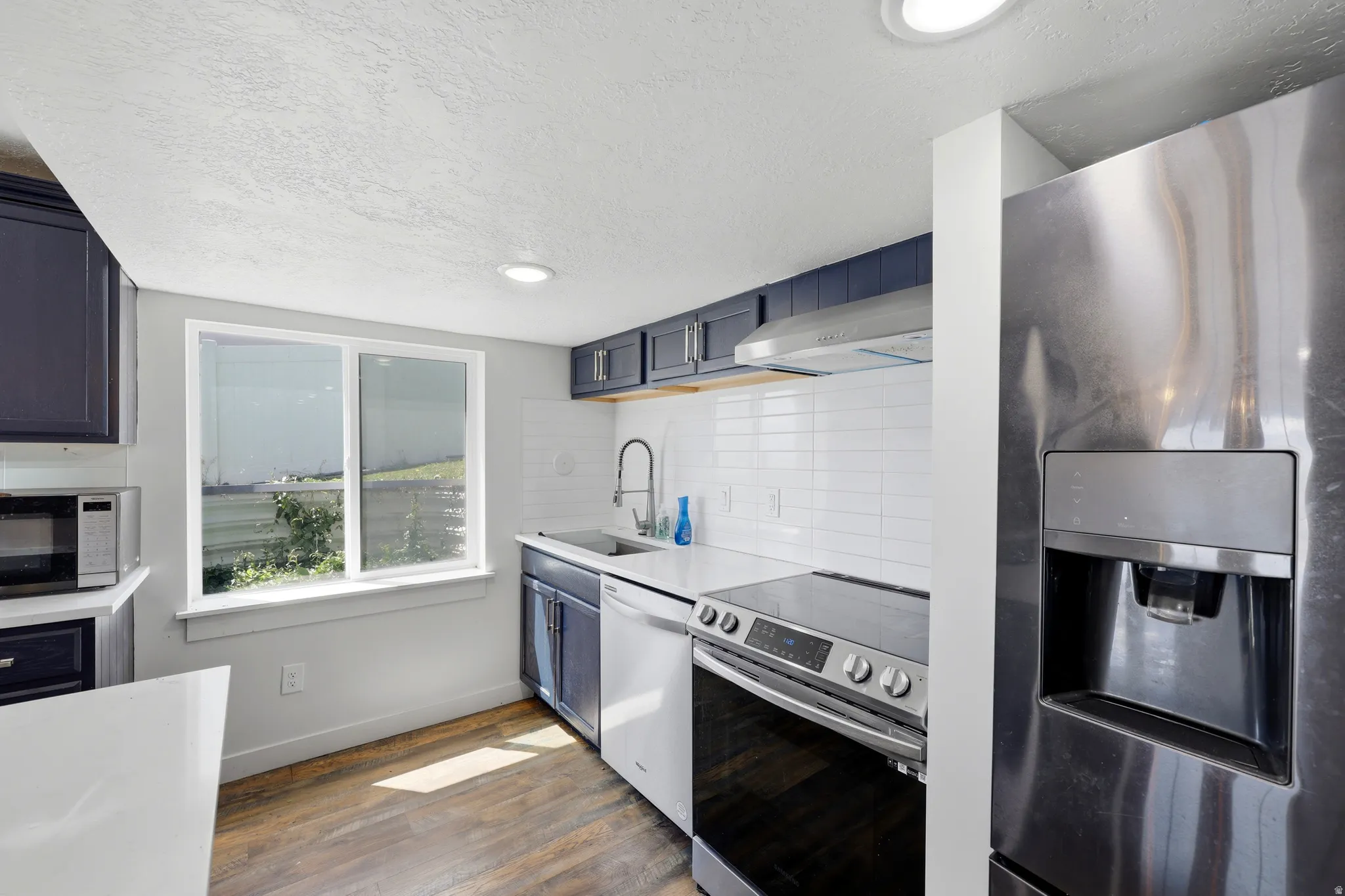 Kitchen featuring dark blue cabinetry, white subway tile backsplash, white countertops, and wood-finish flooring