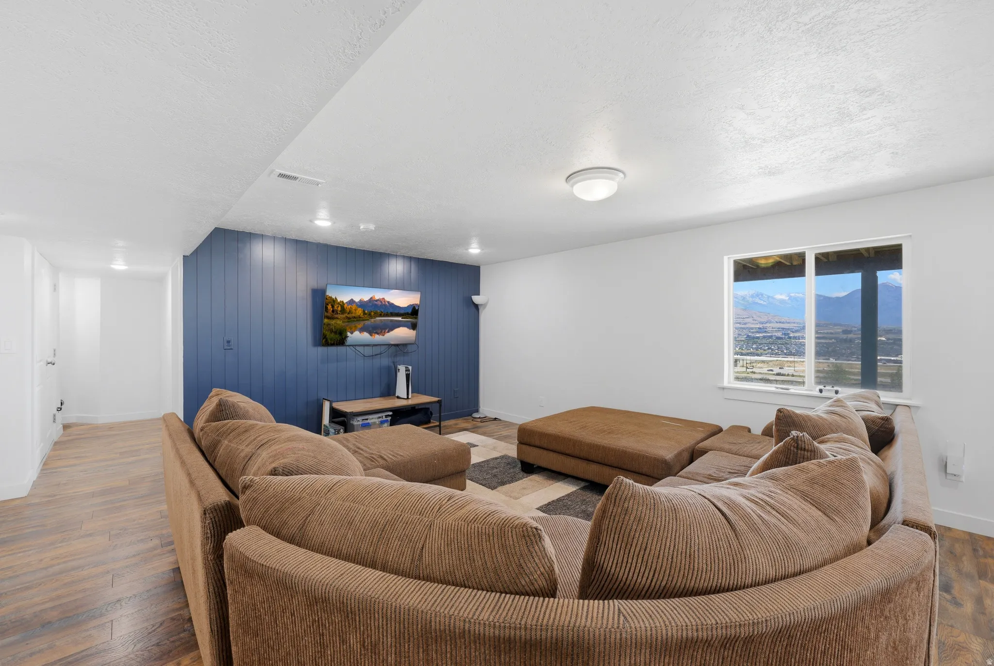Spacious living area featuring a prominent window, plank wood-finish flooring, and a distinctive accent wall with vertical paneling