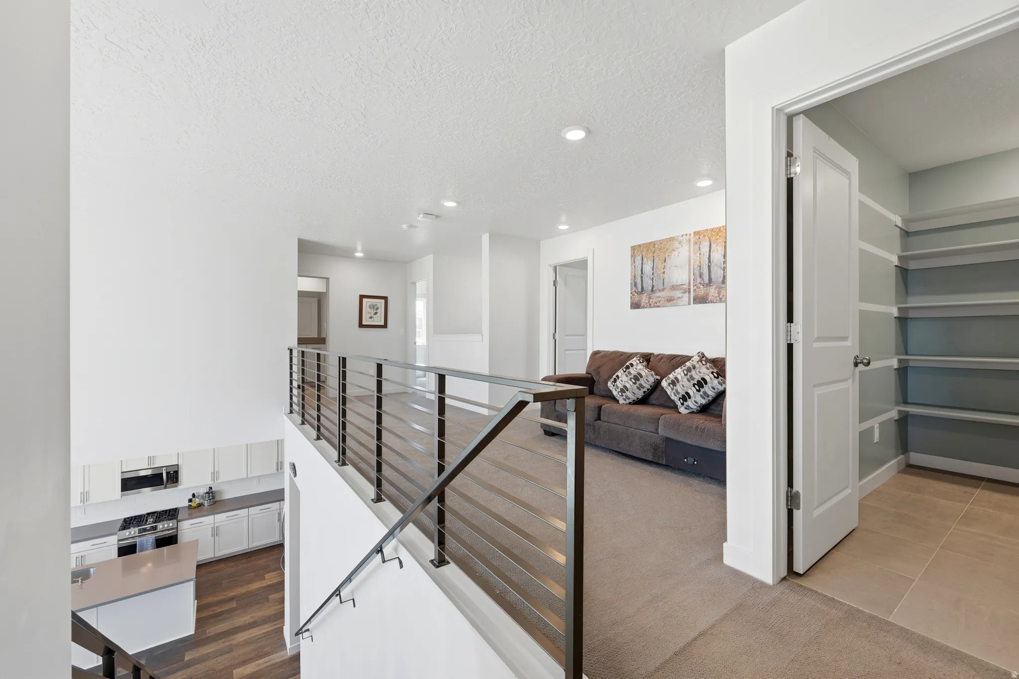 Open-concept floor plan featuring a modern horizontal metal railing, recessed lighting, and a kitchen with white cabinetry and a stainless steel appliance suite