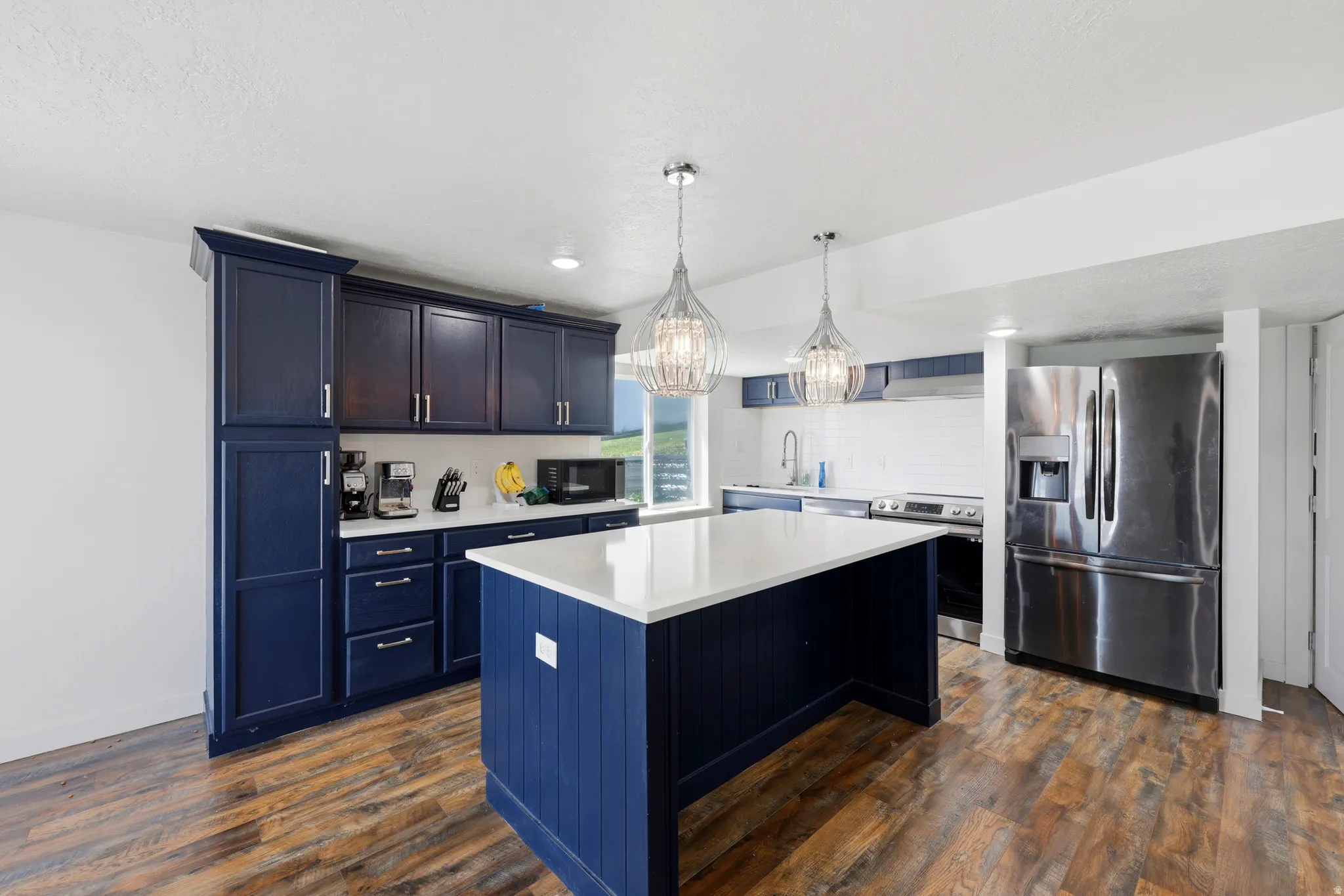 Spacious kitchen featuring dark blue cabinetry, a large kitchen island with a white countertop, and wood-finish flooring