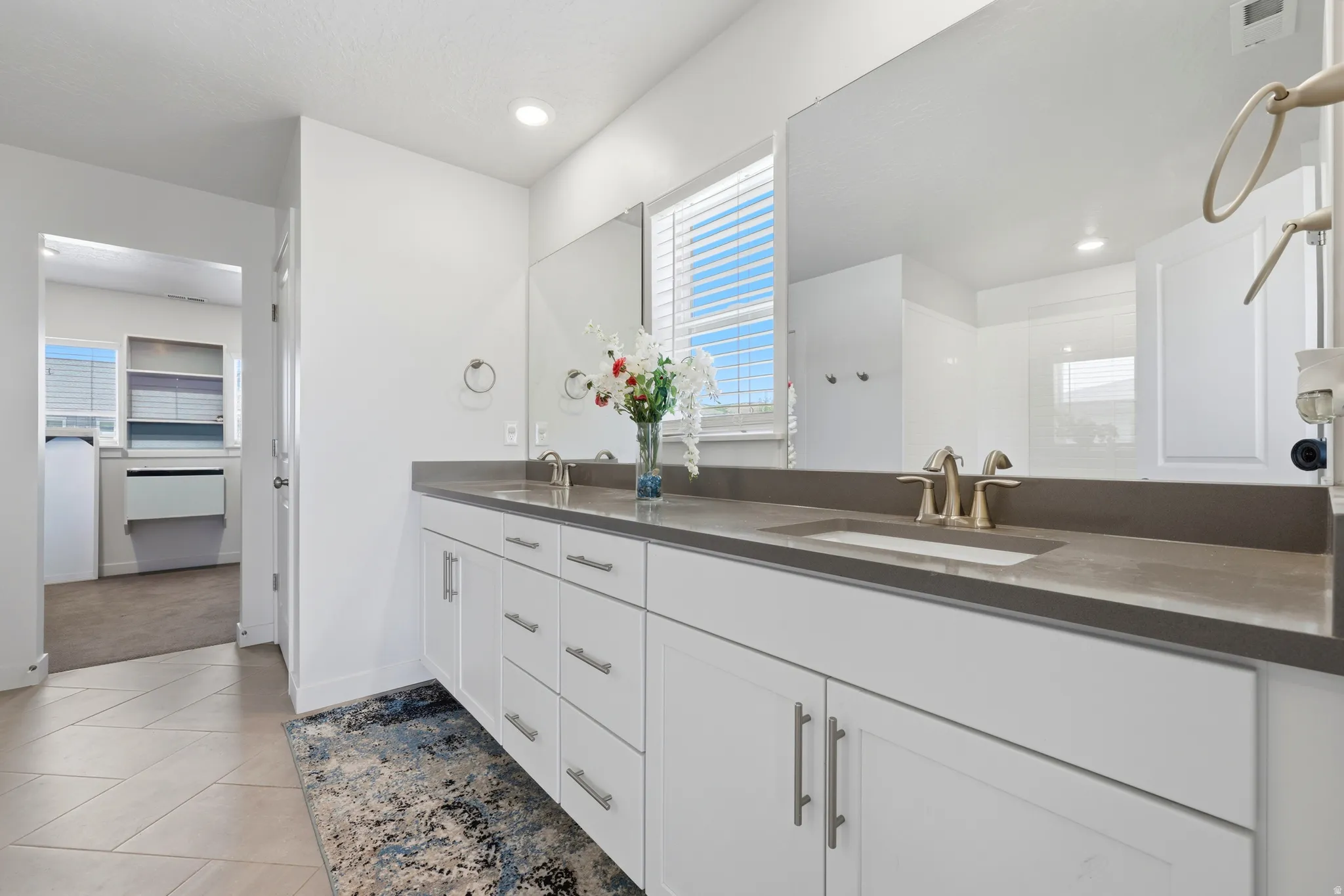Dual vanity with white cabinetry, brushed nickel hardware, and a dark stone countertop featuring two integrated sinks