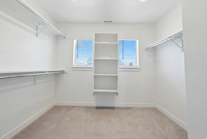 Spacious walk-in closet featuring built-in shelving, two windows with blinds, and ample hanging rod space