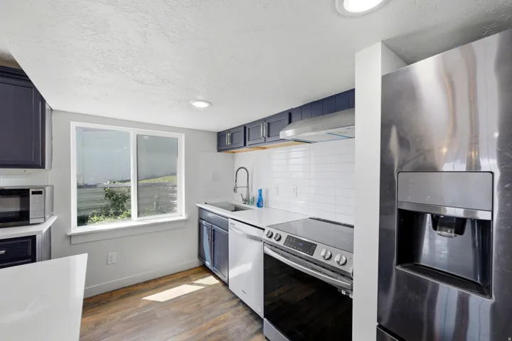Kitchen featuring dark blue cabinetry, white subway tile backsplash, white countertops, and wood-finish flooring